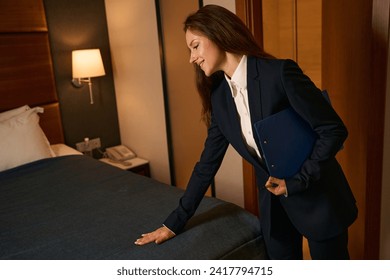 Joyous supervisor checking condition of bedding in guest suite after cleaning