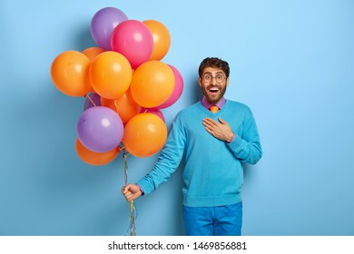 Joyous Surprised Man Being Impressed By Something Positive, Being On Party In Club, Wears Festive Blue Outfit, Holds Airballoons Of Different Colours. People, Joy, Anniversary And Fun Concept