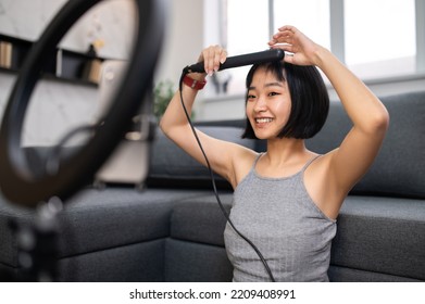 Joyous vlogger curling her hair with a curler - Shutterstock ID 2209408991
