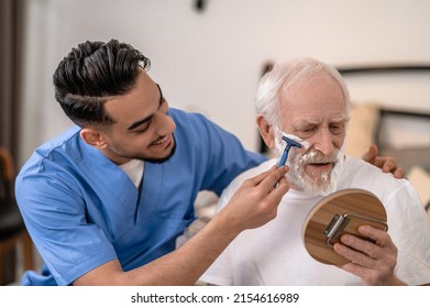 Joyous young man shaving a serious old gentleman