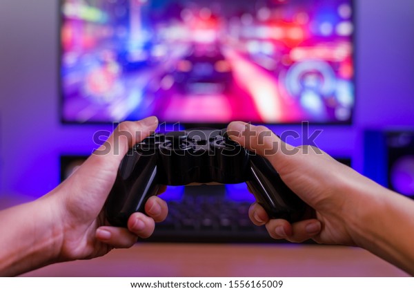 Joypad in hands. Gaming concept.\
Computer display with racing game and rgb light in\
background.