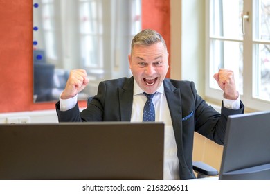 Jubilant businessman celebrating a success at work cheering and pumping the air with his fists