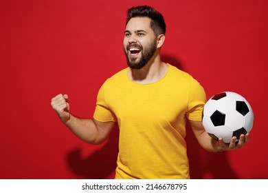 Jubilant fun young bearded man football fan in yellow t-shirt cheer up support favorite team hold soccer ball look aside clenching fists say yes isolated on plain dark red background studio portrait - Shutterstock ID 2146678795