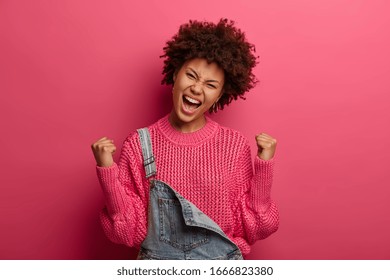 Jubilant overjoyed African American woman celebrates victory, achieves success, exclaims with tiumph, wears sweater, tilts head, poses over pink background. being happy winner. Yeah, I did it! - Shutterstock ID 1666823380