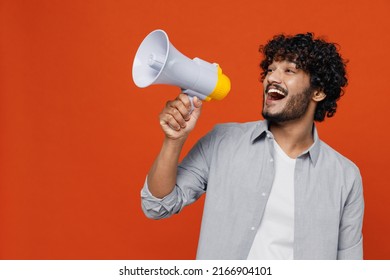 Jubilant overjoyed excited vivid young bearded Indian man 20s years old wears blue shirt hold scream in megaphone announces discounts sale Hurry up isolated on plain orange background studio portrait