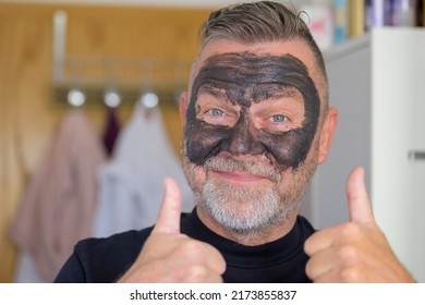 Jubilant Senior Man Doing A Skin Care Treatment Using A Face Mask Smiling And Giving A Double Thumbs Up Of Approval