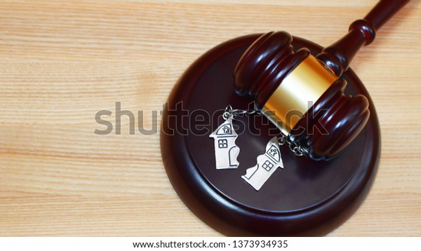 Judge gavel and key chain in shape of two\
splitted part of house on wooden background. Concept of real estate\
auction or dividing house when divorce, division of property, real\
estate, law system.\
