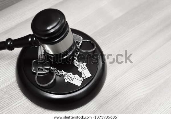 Judge gavel and key chain in shape of two\
splitted part of house on wooden background. Concept of real estate\
auction or dividing house when divorce, division of property, real\
estate, law system.\
