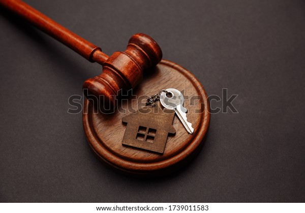 Judge gavel and key chain in shape of two splitted\
part of house on wooden background. Concept of real estate auction\
or dividing house when divorce, division of property, real estate,\
law system