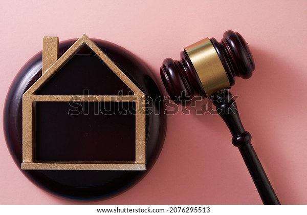 Judge gavel and  model house on pink\
background. Concept of real estate auction or dividing house when\
divorce, division of property, real estate, law\
system