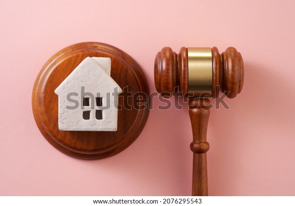 Judge gavel and  model house on pink\
background. Concept of real estate auction or dividing house when\
divorce, division of property, real estate, law\
system