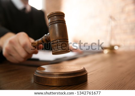 Judge with gavel at table in courtroom, closeup. Law and justice concept