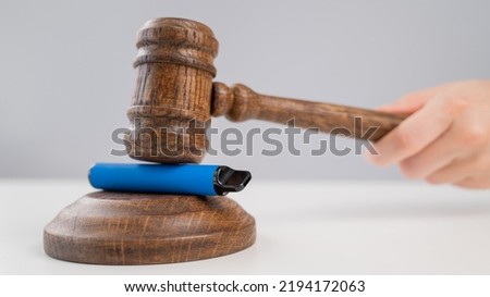 Judge hammering disposable vape with referee's gavel on white table. 