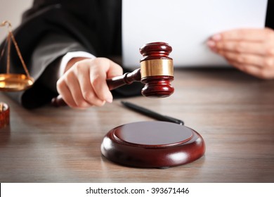 Judge hitting gavel with paper at wooden table closeup