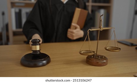 Judge holding book in courtroom with gavel and scales of justice on the desk - Powered by Shutterstock