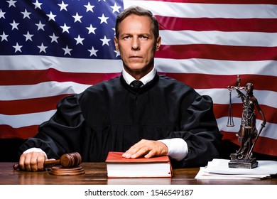 Judge In Judicial Robe Holding Gavel And Putting Hand On Book 