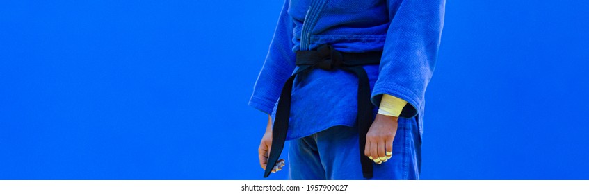Judo fighter poses in blue kimono with black belt. Japanese judo and jiu jitsu
