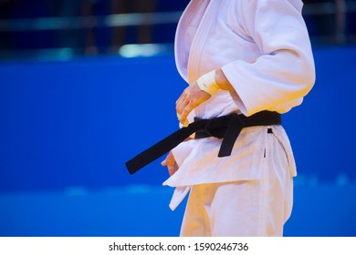 Judo fighter poses in white kimono with black belt. Japanese judo and jiu jitsu