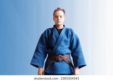 Judo girl with brown belt. A judoka teenager fighter poses in a blue kimono on a plain background. Japanese martial art. The process of martial arts training. Healthy lifestyle, sports concept