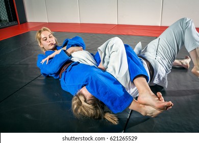 Judo, Jiu Jitsu. Two Women Are Fighting On Tatami. Blue And White Kimano. Painful Reception. Ground Floor