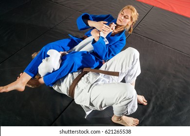 Judo, Jiu Jitsu. Two Women Are Fighting On Tatami. Blue And White Kimano. Painful Reception. Ground Floor