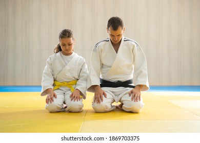 Judo master and young yellow belt judo girl in white judogi kneeling 