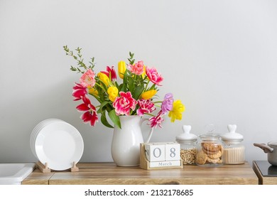 Jug With Beautiful Flowers And Cube Calendar With Date 8 MARCH On Kitchen Counter Near Light Wall. International Women's Day Celebration