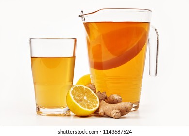 Jug and glass filled with fresh kombucha made with fermented sweetened black tea and served with lemon and root ginger over white viewed from the side