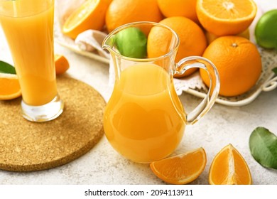 Jug and glass of tasty orange juice on light background, closeup