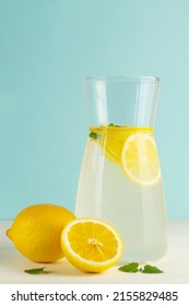 jug of lemonade with lemon.Summer refreshing cocktail with lime and mint on blue background. Fresh summertime iced drink with yellow citrus and green leaves in glass and jug. copy space. vertical
