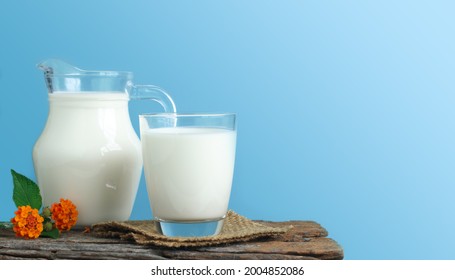 A jug of milk and glass of milk on a wooden table on a blue background. - Shutterstock ID 2004852086