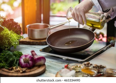 Кувшин наливает жидкость на сковороду. Зеленый салат и фиолетовый лук. Сковорода прогревается. Нужно немного оливкового масла.