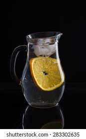 Jug With Water, Ice And One Slice Of Orange On Black Background