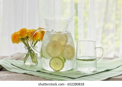 A Jug Of Water And Lemon And Lime And A Bouquet Of Dandelions