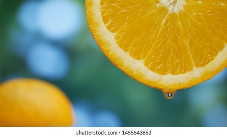 Juice drops flows down on orange fruit on garden background
