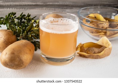 Juice from potatoes in a glass near a whole potato and shkarlupy in a bowl. - Shutterstock ID 1337543522