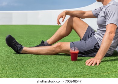 Juice smoothie sport man relaxing enjoying post workout morning breakfast sitting on outdoor grass at home or fitness gym. Athlete drinking red fruit smoothie drink. - Powered by Shutterstock