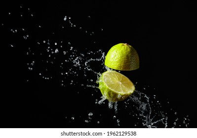 Juice splashes out of a cut lime on a black background.