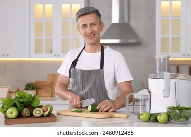 Juicer and fresh products on white marble table. Smiling man cutting cucumber in kitchen - Powered by Shutterstock