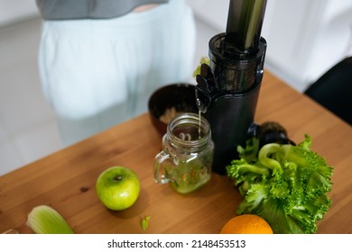 The Juicer Stands On A Wooden Table And Pours Celery Juice Into A Glass Top View