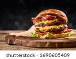 Juicy American burger, hamburger or cheeseburger with two beef patties, with sauce and basked on a black background. Concept of American fast food. Copy space