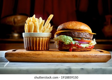 Juicy and appetizing burger with tomatoes, lettuce, cucumber, melted cheese and onions with brioche bun served on a wooden board with fries - Powered by Shutterstock