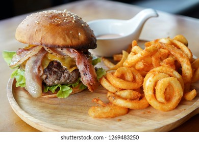 Juicy Beef Burger With America Cheese And Bacons On Top Served With Curly Fries On Wooden Board