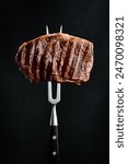 A juicy beef ribeye steak on a fork. Grilled steak. On a black background.