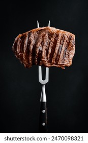 A juicy beef ribeye steak on a fork. Grilled steak. On a black background.