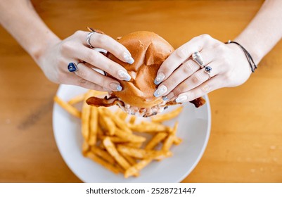 A juicy burger with crispy fries, held in a person's hands. The burger bun is slightly open, revealing delicious toppings. Perfect for fast food, comfort food, and restaurant menus - Powered by Shutterstock