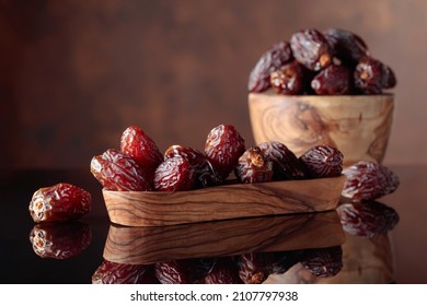 Juicy dates in wooden dishes on a black reflective background. Copy space.
