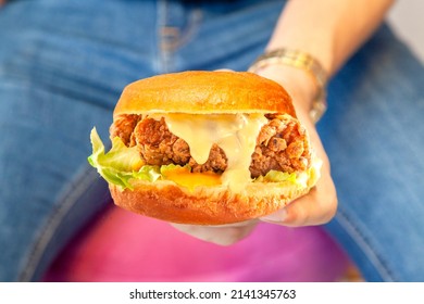 Juicy Fried Chicken Street Burger Holding In One Hand Closeup With Person Wearing Blue Jeans And Black Shirt In The Background