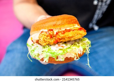 Juicy Fried Chicken Street Burger Holding In One Hand Closeup With Person Wearing Blue Jeans And Black Shirt In The Background