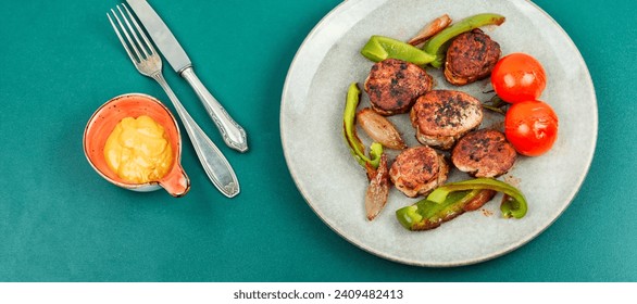 Juicy fried meat medallions with stewed vegetables and sauce on a plate. Top view.